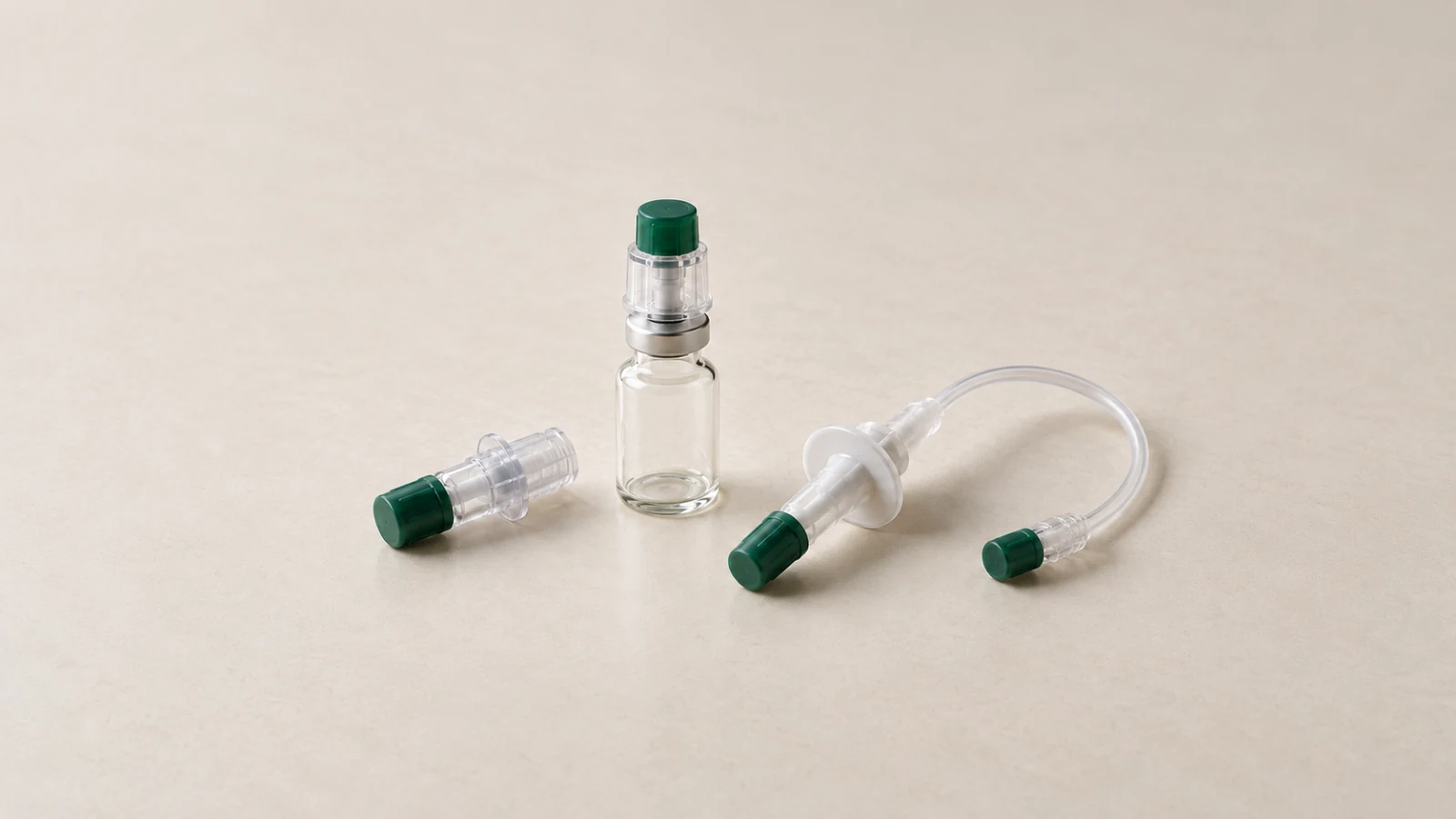 Illustrative still life of capped translucent transfer adapters and short clear tubing beside an unlabeled empty glass vial on a warm off-white surface.