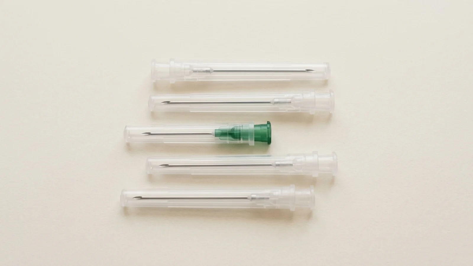 Text-free catalog still life of sterile hypodermic needles with translucent protective caps on a warm off-white background