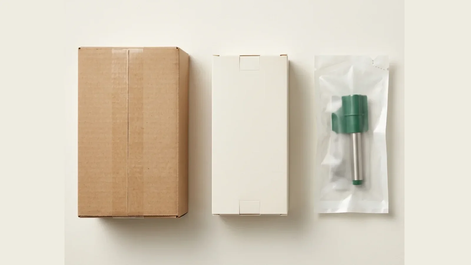 Unbranded corrugated shipping carton, cream protective carton, and translucent sterile pouch with a forest-green and stainless consumable on a warm off-white field